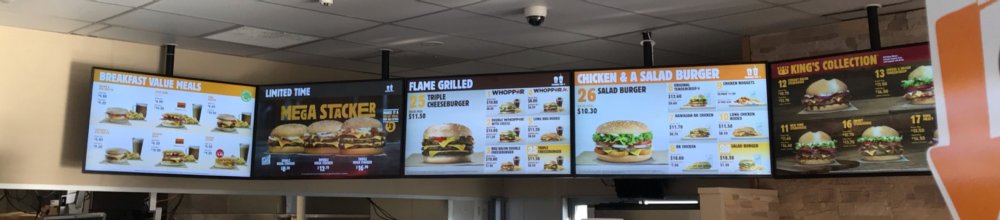 Multiple screens above the serving area show the menu of the fast food restaurant.