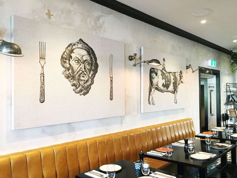 Large acoustic panels with printed restaurant themed artwork, hung on a wall behind tables in a restaurant
