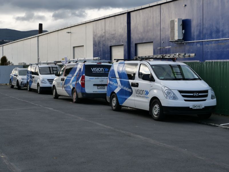 Three work vans and one hatchback with Vision branding parked behind St. Patrick's Basilica