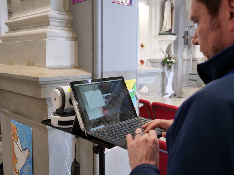 Neville works on a laptop to set up the new camera system at St. Patrick's Basilica, in front of a column