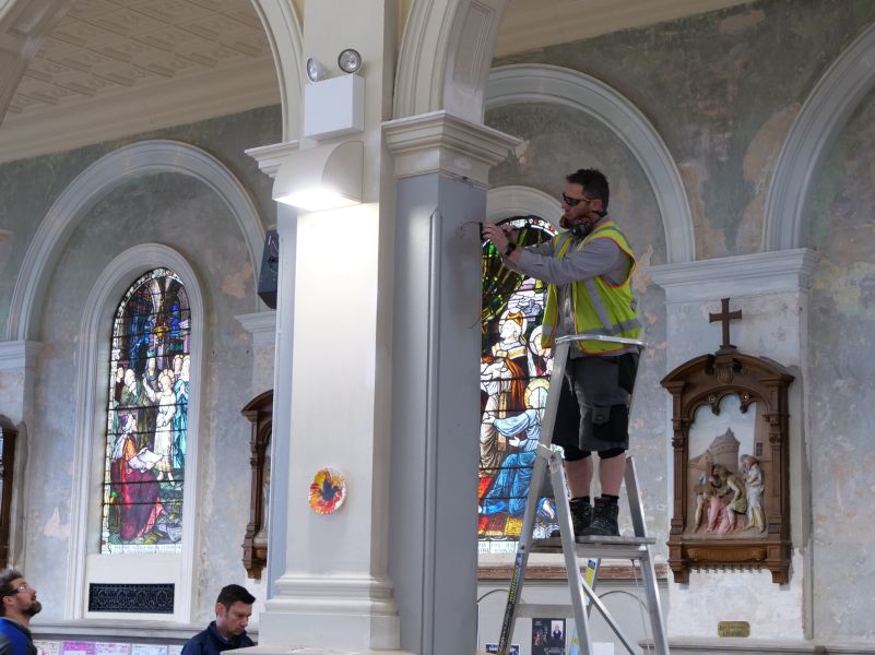 Technician standing on a ladder in the basilica, feeding cable into a wall